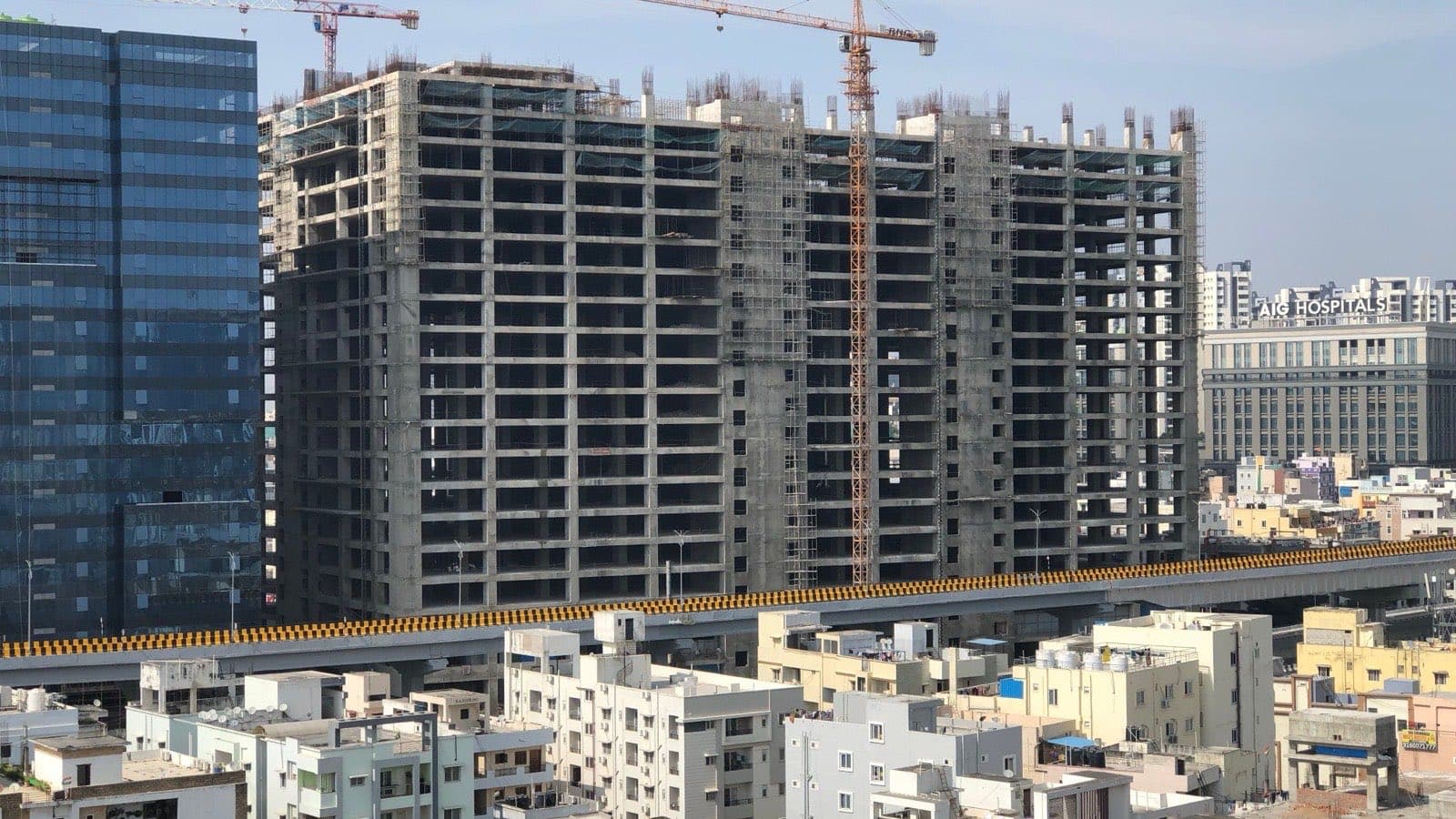 Residential towers under construction with cranes on top, beside a crowded city skyline